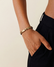 Hand wearing a gold bracelet on a plain background