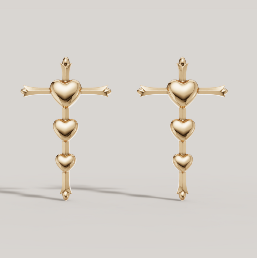 Pair of gold earrings with heart and cross design on a light gray background